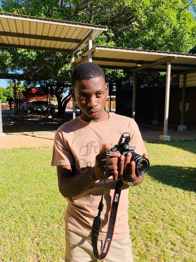 Kudumo Kupembona Andreas holding and operating a camera outdoors