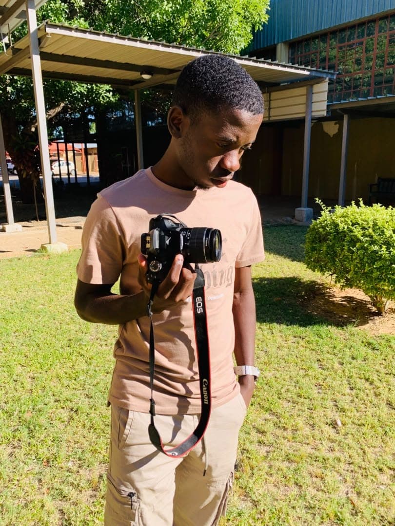 Kudumo Kupembona Andreas holding a camera in an outdoor side portrait